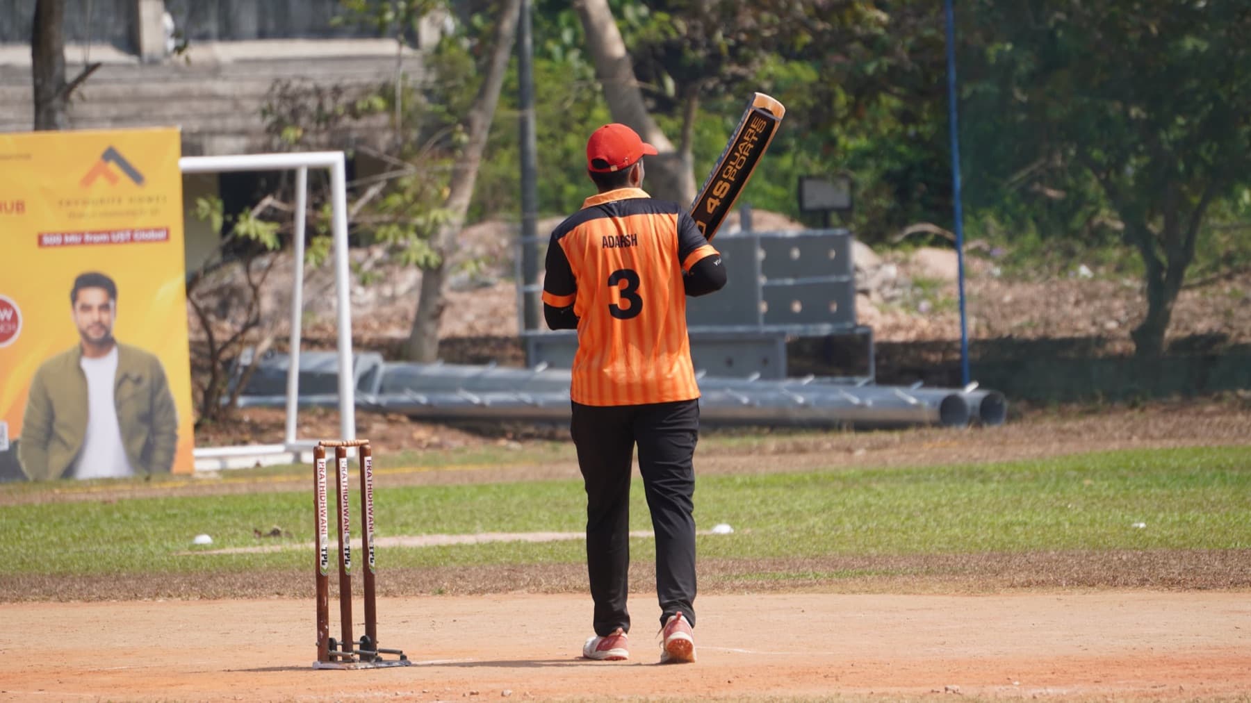 Adarsh walking out to bat in an orange number 3 jersey